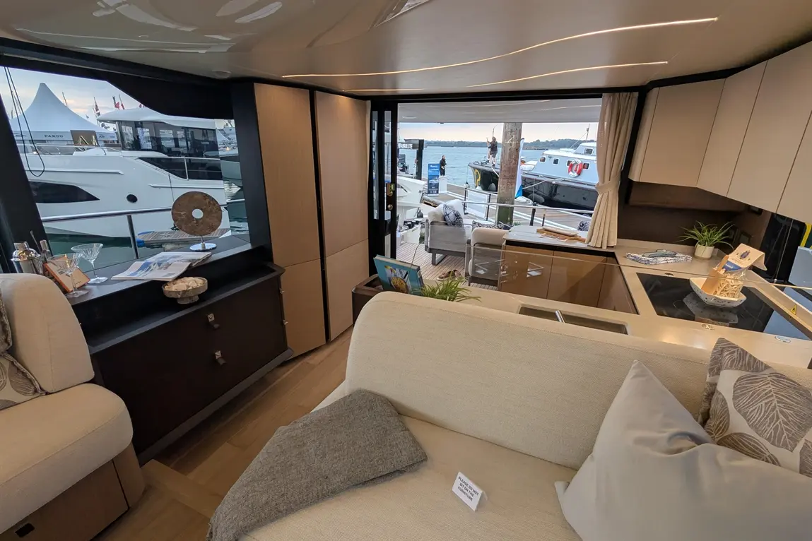 Luxurious yacht interior featuring a seating area, kitchen, and large window showcasing boats and waterfront.